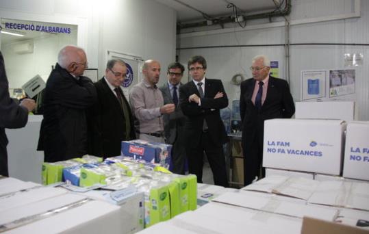 Imatge general del president de la Generalitat, Carles Puigdemont, seguint les explicacions al magatzem del Banc dels Aliments, amb caixes d'aliments 