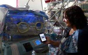 Una mare al costat del seu fill a l'UCI de Neonatologia de BCNatal, mostrant la pantalla del mòbil on pot veure en qualsevol moment el seu nadó . ACN