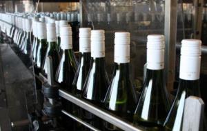 Detall de desenes d'ampolles de vi negre sense etiquetar, en plena cadena d'embotellament