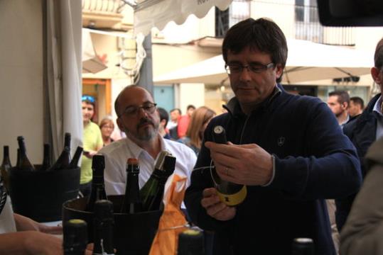 El president de la Generalitat, Carles Puigdemont, agafa amb les mans una ampolla en passejar per la Fira del Vi de Vilanova i la Geltrú. ACN