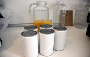 Pla general de diverses llaunes amb suc de taronja congelat de l'estudi Citrus, en primer terme, davant d'un got i una gerra plens. ACN