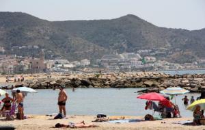 Pla general d'una platja de Sitges amb diversos banyistes, amb la icònica església de 'La Punta' al fons. ACN