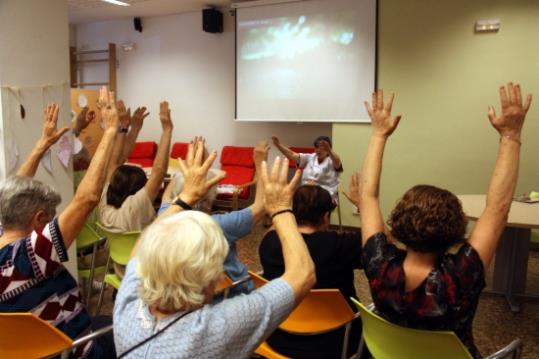 Un grup d'avis aixequen les mans seguint les instruccions d'una terapeuta en un taller de psicomotricitat a l'AFAB per a malalts d'Alzheimer