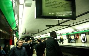 Usuaris esperant el metro a la parada Catalunya de la L3, amb un cartell anunciant la vaga a la pantalla superior. ACN