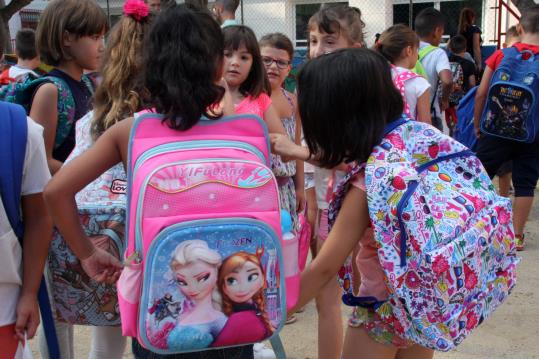 Dues nenes, d'esquenes, llueixen grans motxilles al matí de l'escola mentre es retroben amb les amigues en el primer dia de curs. ACN