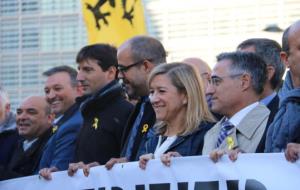 El president de l'ACM, Miquel Buch, i la de l'AMI, Neus Lloveras, sostenen la pancarta demanant des de Brussel·les l'alliberament de presos polítics. 