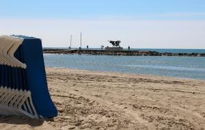 Pla general d'una platja de Vilanova, amb gandules de lloguer en primer terme i l'escultura de la Pasífae al fons