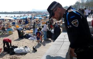 Pla mig d'un agent de la Policia Local de Sitges, mirant a través de la barana d'accés a la platja mentre un grup de manters són a la sorra. ACN