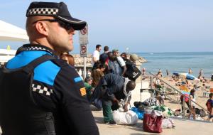Pla mig d'un agent de la Policia Local de Sitges, mirant a través de la barana d'accés a la platja mentre un grup de manters són a la sorra