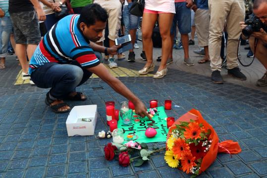 Pla sencer d'un home encenent una espelma a l'ofrena floral del centre de les Rambles el 18 d'agost de 2017. ACN