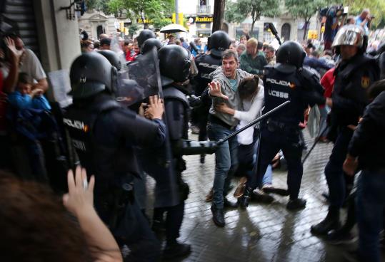 Un home intenta protegir una dona dels cops de porra d'agents antidisturbis de la policia espanyola l'1 d'octubre d'aquest 2017. ACN