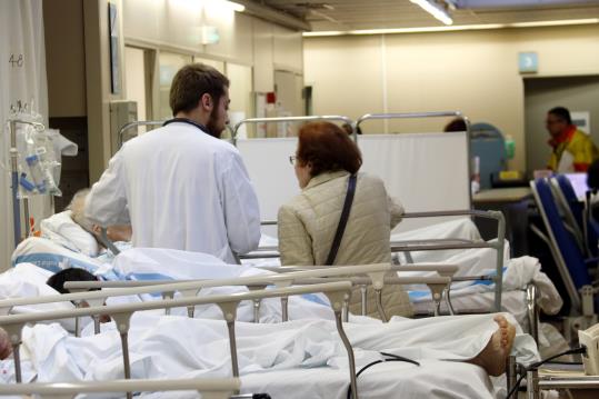 Un metge atenent un pacient amb la companyia d'un familiar a l'Àrea d'Urgències Mèdiques de la Vall d'Hebron de Barcelona, on alguns pacients esperen 