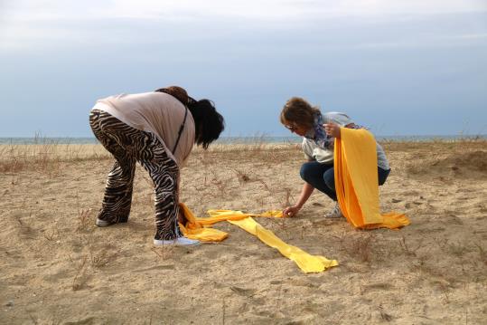 Dues dones estenen teles de tovallola groga en forma de creu a la platja de Mataró, el 27 de maig de 2018. ACN