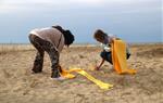 Dues dones estenen teles de tovallola groga en forma de creu a la platja de Mataró, el 27 de maig de 2018. ACN