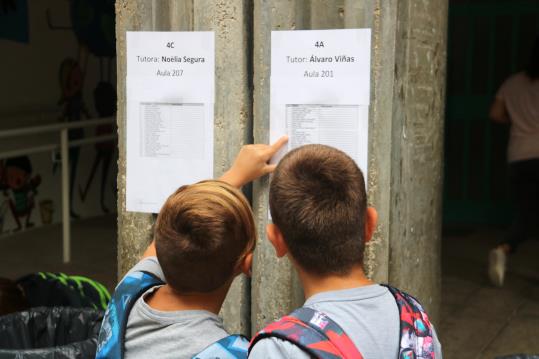 Pla curt de dos nens observant la llista d'alumnes per aula a l'entrada de l'escola de Ferreries. ACN