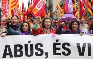 Pla mig de tres dones representants de CCOO i UGT a la capçalera de la manifestació aguantant la pancarta 'No és abús, és violació' del Primer de Maig