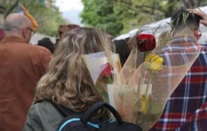 Una dona d'esquena porta dues roses vermelles i una groga a la motxilla. ACN