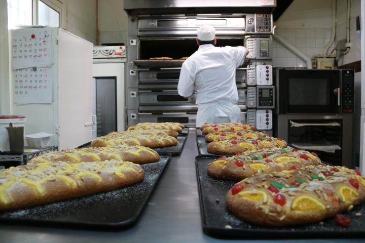 Pla general de coques de Sant Joan amb un pastisser obrint el forn en un segon pla a l'obrador de la pastisseria Lis de Barcelona. ACN