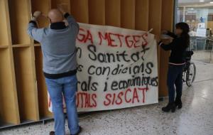 Pla mitjà de dos dels membres del comitè d'empresa del sindicat de Metges de Catalunya penjant una pancarta reivindicativa de la jornada de vaga. ACN