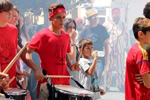 Pla mitjà lateral d'un dels menors estrangers no acompanyats acollits a Cubelles, tocant el timbal durant una cercavila de la Festa Major