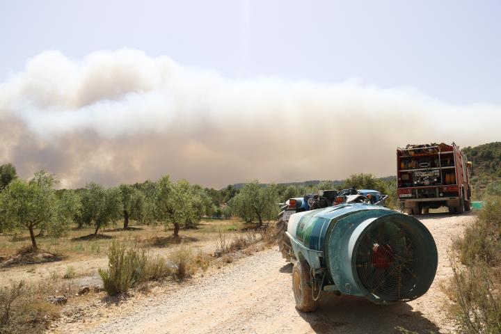 Pla sencer d'un camí de Bovera on es veu el fum de fons i hi ha un camió de bombers i una cisterna d'aigua. ACN