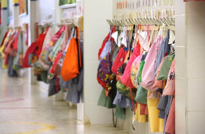 Aspecte d'un passadís d'escola, buit d'alumnes, amb els penjadors carregats amb les bates i les motxilles dels petits. ACN