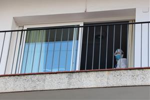 Detall del balcó d'una habitació de la residència Calafell Park de Segur de Calafell, amb un treballador amb EPI sortint per la porta. ACN