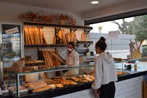 Interior d'una botiga d'Igualada amb una dependenta amb mascareta posant una barra de pa dins una bossa, el 13 de març del 2020. ACN