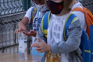 Pla detall de dos alumnes de primària rentant-se les mans amb gel hidroalcohòlic a l'accés de l'escola Sant Llàtzer de Tortosa. ACN