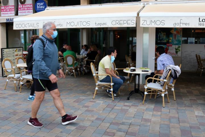 Pla general de la terrassa d'una cafeteria a Calafell Platja mentre un home passeja amb mascareta. ACN