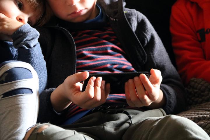Pla mitjà de tres nens petits mentre miren el telèfon mòbil. Imatge publicada el 8 de novembre del 2020. ACN