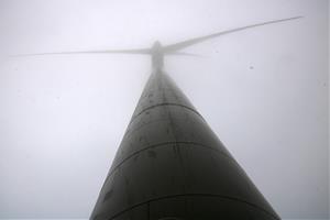 Pla obert on es pot veure un aerogenerador des de la base, envoltat de boira, al parc eòlic de la Serra de Montargull. ACN