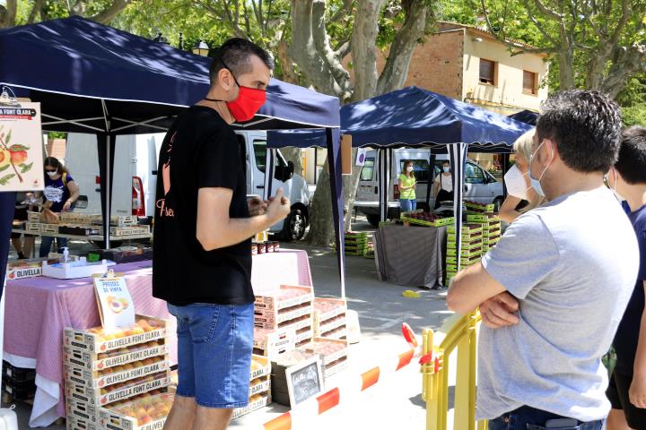 Un productor atenent clients al Mercat del Préssec d'Ordal, separats per una tanca per preservar la distància de seguretat. ACN