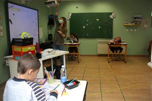 Una professora amb mascareta i utilitzant el projector de l'aula i un grup d'alumnes distanciats entre ells. ACN / Albert Lijarcio