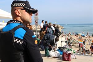 Pla mig d'un agent de la Policia Local de Sitges, amb manters al fons recollint els seus productes. Imatge del 14 d'abril de 2017. ACN