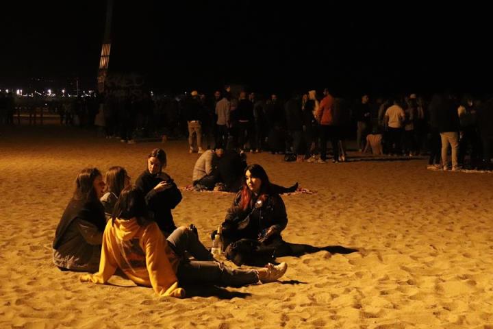 Pla obert d'un grup d'amics asseguts a la platja de la Barceloneta. ACN