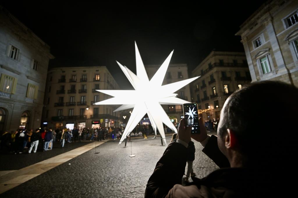 Una persona fotografia l'estrella que configura l'element principal de la instal·lació nadalenca 'Origen' a la plaça Sant Jaume de Barcelona. ACN