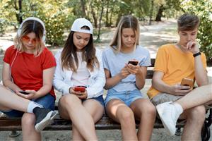 Adolescents asseguts en un banc al parc, centrats en els seus telèfons mòbils. Freepik