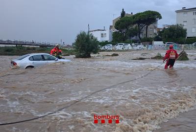 Dos bombers fent maniobres al mig d'una riera, amb un fort cabal, on va quedar un cotxe encallat. ACN / Bombers